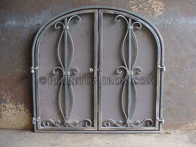 Wrought iron arched top fireplace doors with a mesh fire screen featuring a gathered scroll pattern centered on each panel.