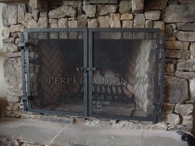 Unembellished fireplace screen with textured steel frame in front of rustic fireplace mantel with mesh fire screen.