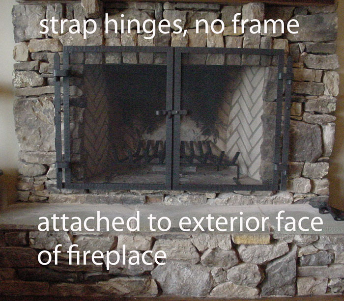 A rough stone fireplace with a frameless, black, double-door screen with strap hinges directly mounted to the stone surround.