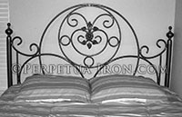 Custom fabricated decorative iron headboard with sweeping, interlocking circular design. The circles are braced with a few curled elements. The centerpiece has a minimal floral pattern suspended by small circles.
