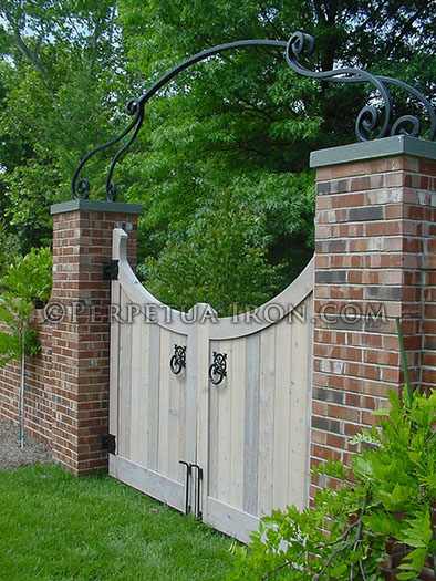 Heavy iron garden arch over a wooden gate.