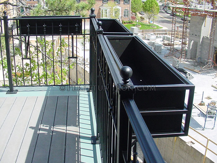 A fabricated steel flower box hanging on a balcony railing.