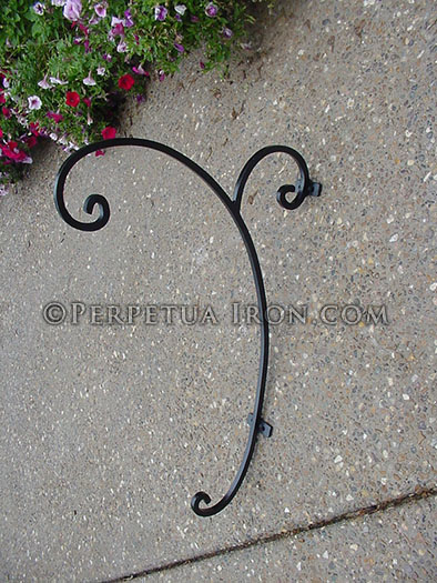A decorative iron plant hanger mounted to a cancrete wall.
