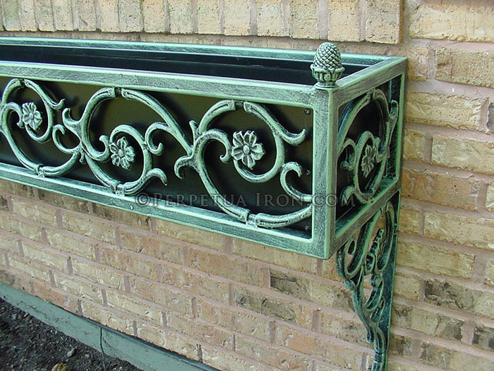 a wrought iron window boxlcose up detail showing a copper oxide patina and swirled flower design.