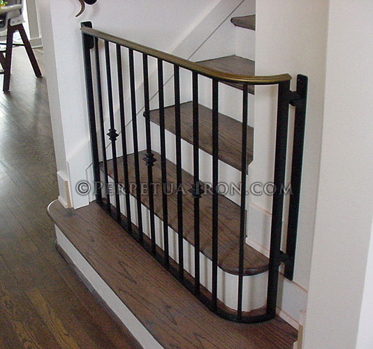 Custom iron baby gate that curves around the bottom of the second step created in a traditional design and a custom black and brass finish.