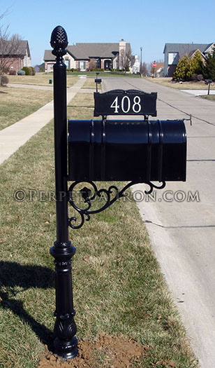 Tightly framed view of a decorative iron column mailbox post with numbers mounte on top of the post.