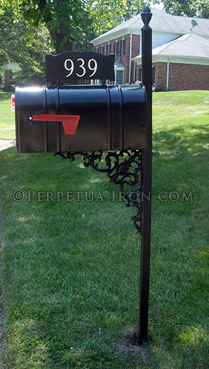 A large scale ornamental iron mailbox post with a symetrical bracket and traditional paisley design.