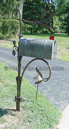 A wildly creative hand forged mailbox post with big swooping, organic curves with a mottled patina on the mailbox.
