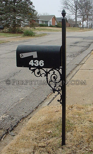 A medium sized decorative iron mailbox on a street with cracked asphault and no sidewalks.