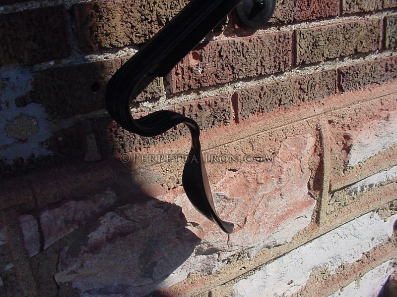 Hand forged leaf railing end against red brick background.