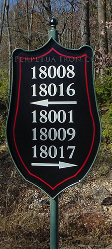 Custom made iron sign for a subdivision post painted green, sheild inspired shape painted black with red pinstripe line and white numbers with awwors pointing left and right.